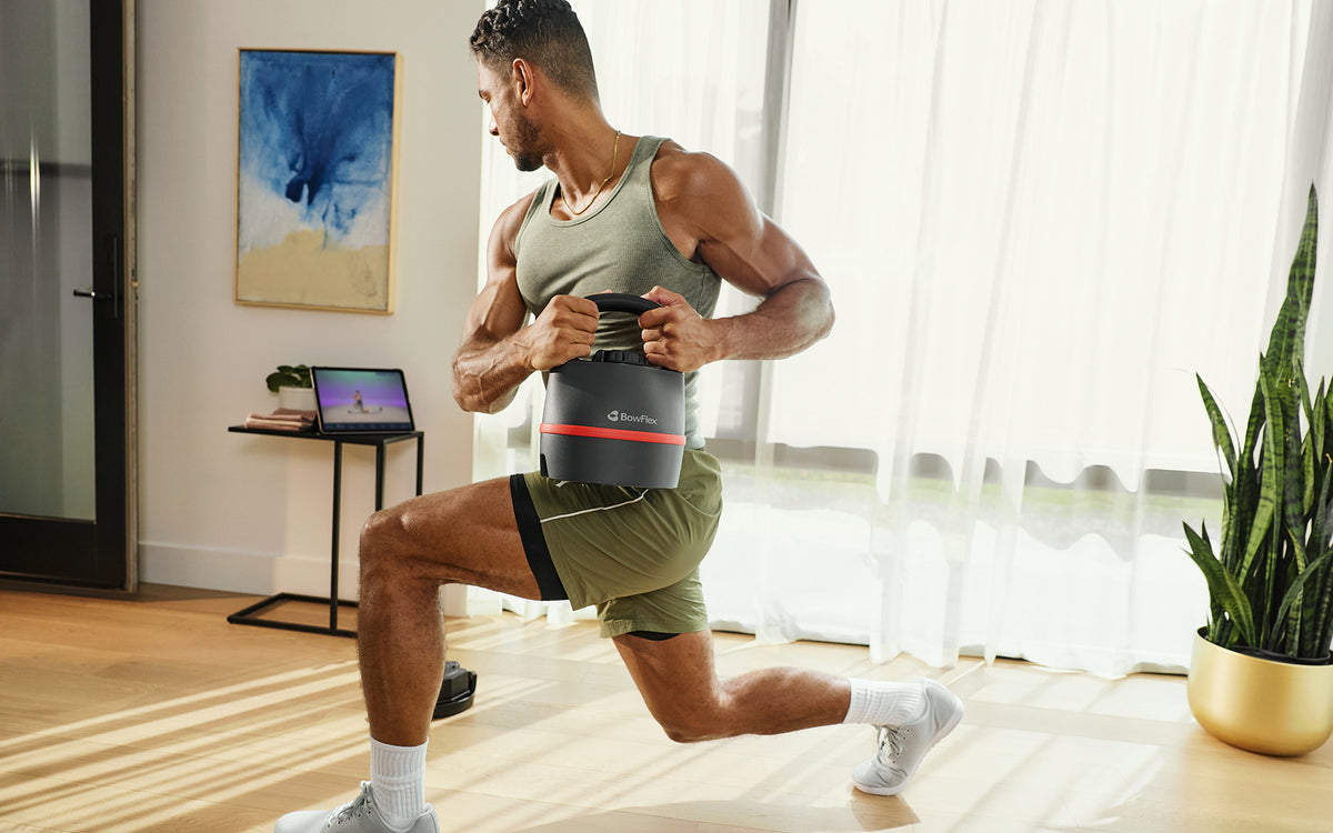 A man in a home gym setting performs a lunge while holding a BowFlex SelectTech 840 Kettlebell.