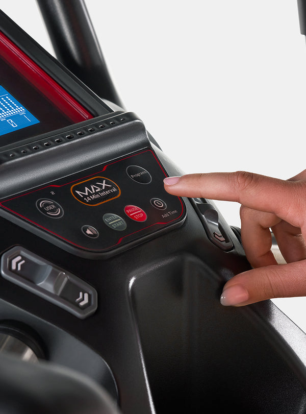 A finger hovering over the Max 14-Minute Interval button on the BowFlex Max Trainer M6 console.