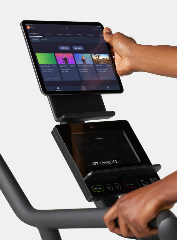 Hand placing a tablet with JRNY app screen displayed onto the BowFlex Max Trainer SEi media shelf.